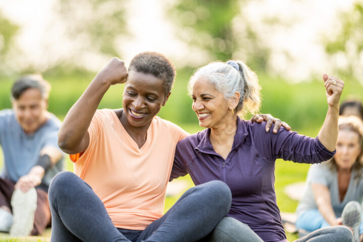 Two senior women at outdoor exercise class smiling and flexing.